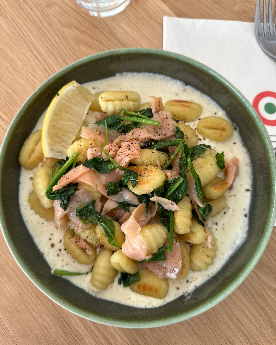 Assiette de gnocchis au saumon et aux épinards, accompagnés d’une sauce crémeuse et d’un quartier de citron.